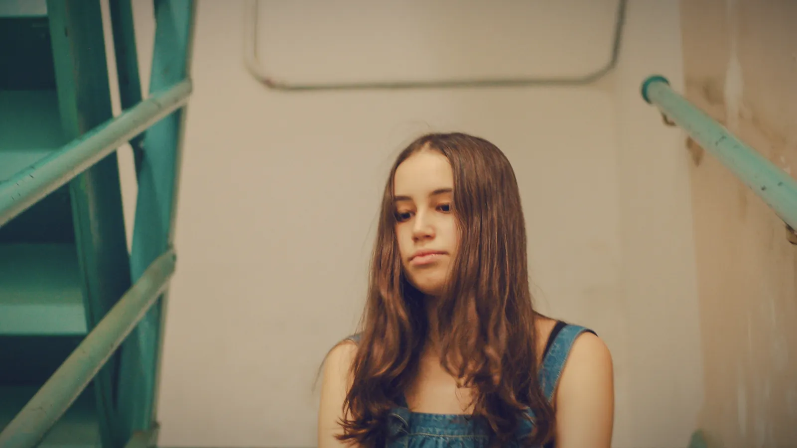A young teenage girl standing in a stairwell with an unimpressed, fed-up look