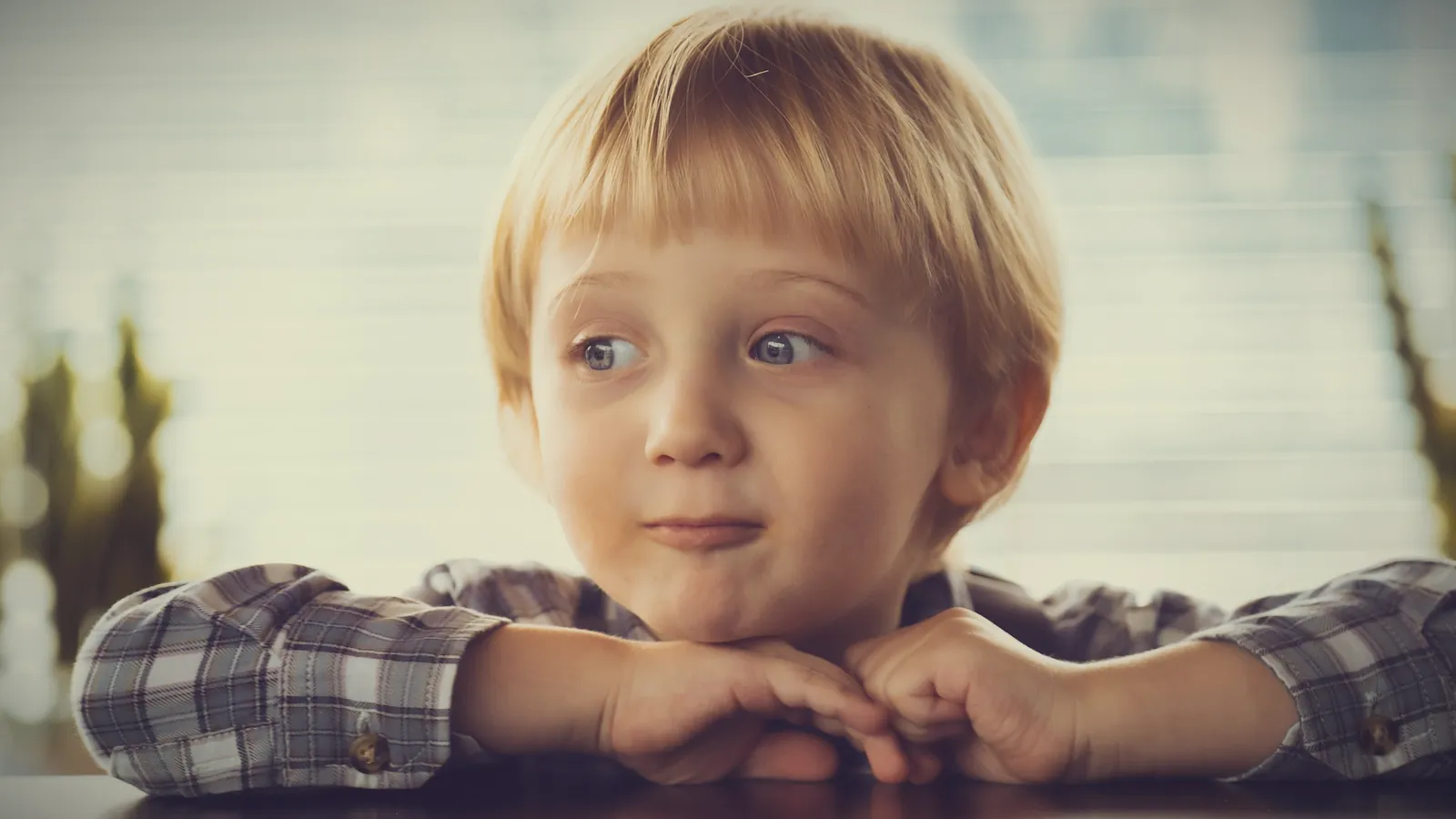 A little blond boy at the table with his chin on his hands and a sheepish, caught-out look