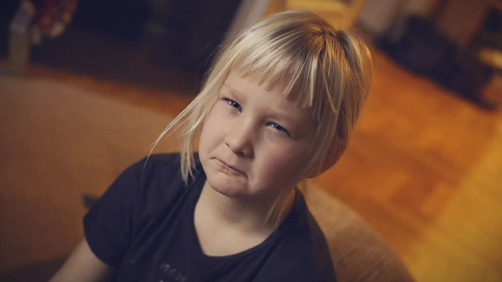 A young girl with blonde bangs pulling a sulky, unimpressed face at home