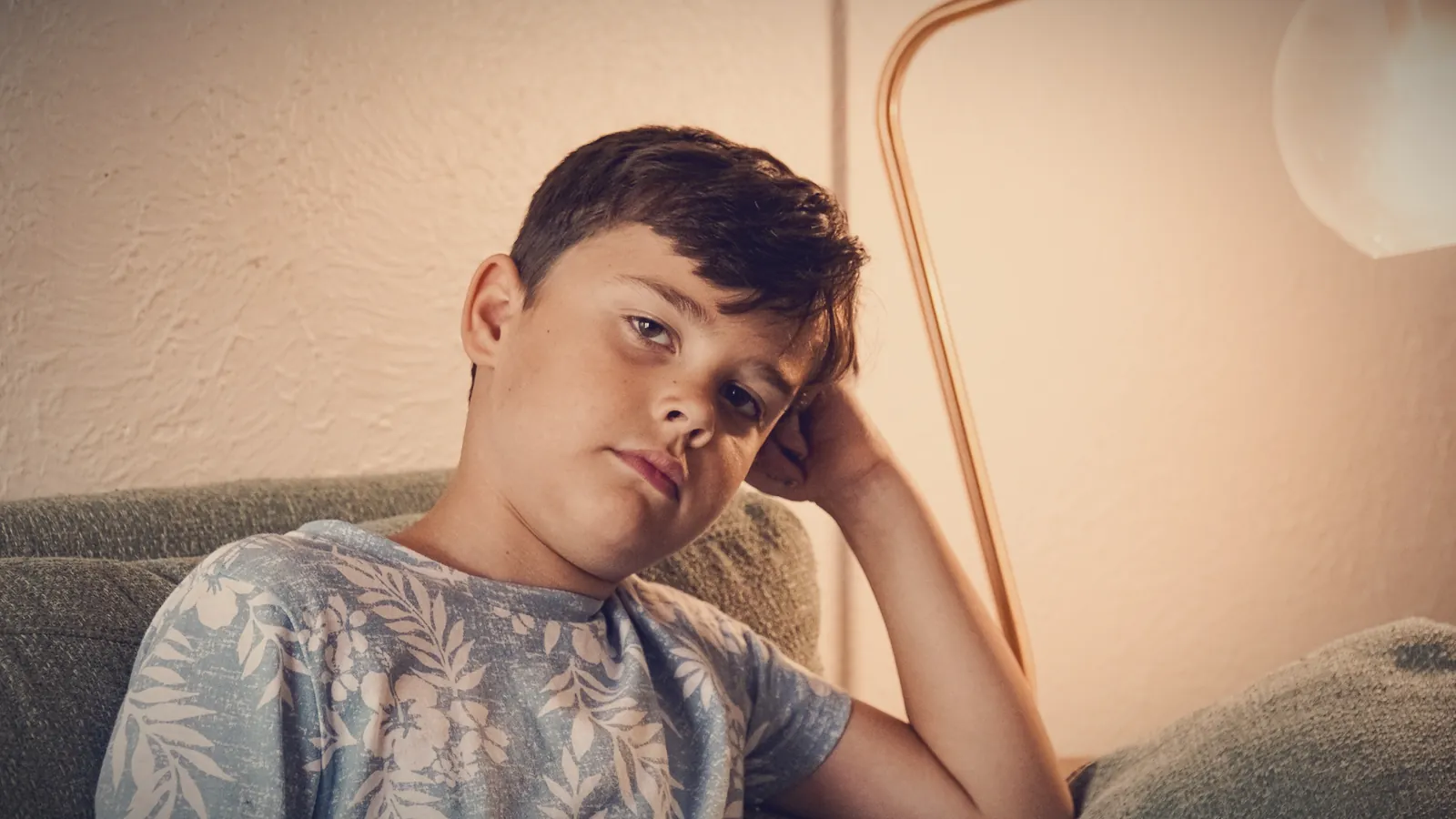 A boy slouched on the sofa, head propped on his hand, with a bored, unimpressed look
