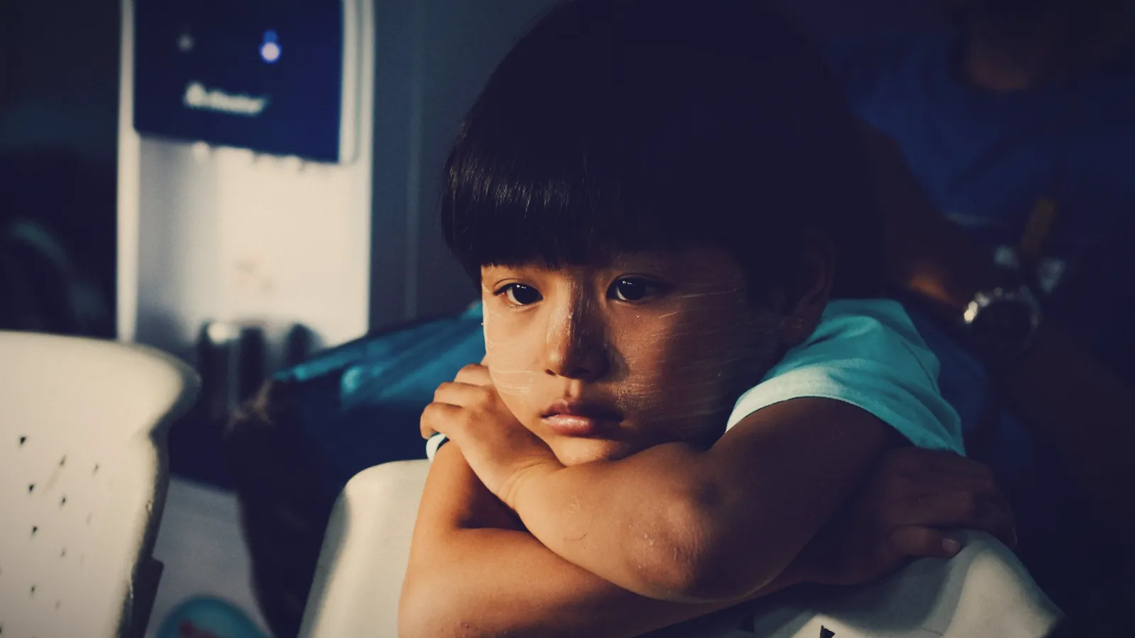 A boy resting his chin on his folded arms with a sulky, indifferent look