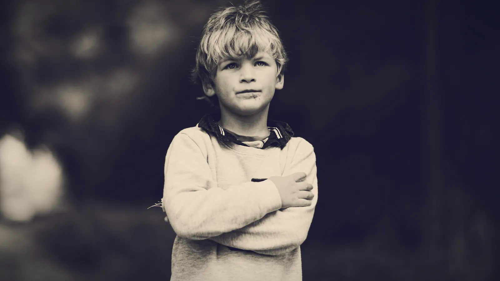 A young boy standing with his arms crossed and a stubborn look