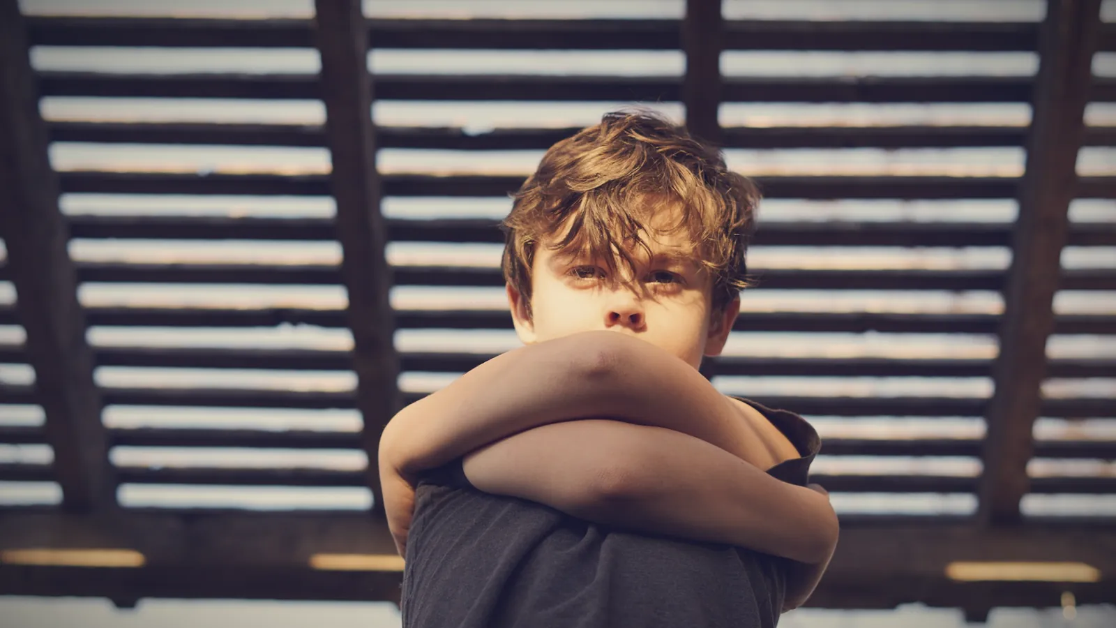 A boy with his arms crossed, looking at the camera with a stubborn expression