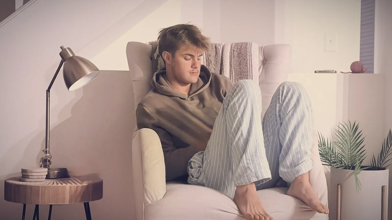 A teenage boy curled up in an armchair in a hoodie, tuned out and avoiding eye contact