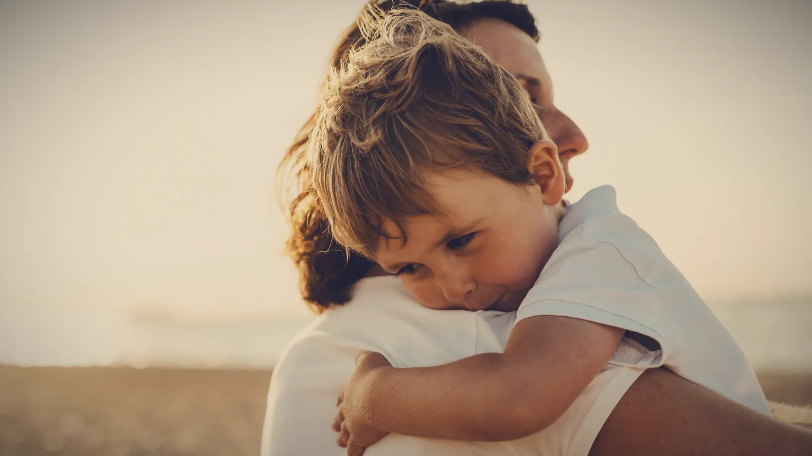 A young boy hugging his parent tightly, resting his head on their shoulder