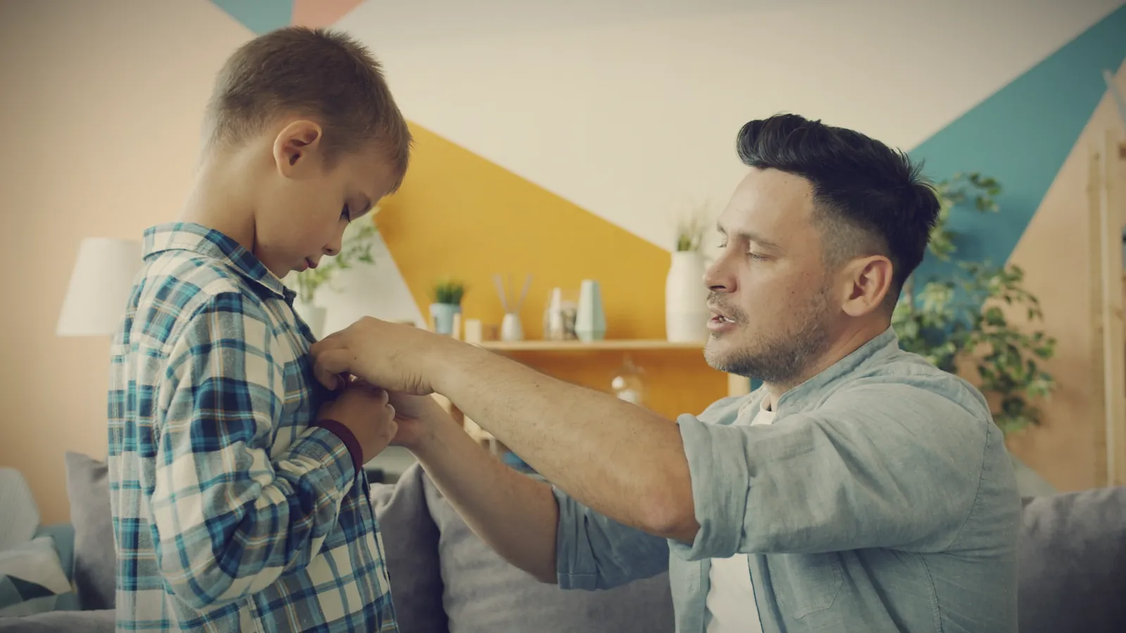 A father talking calmly with his young son while helping him button his shirt