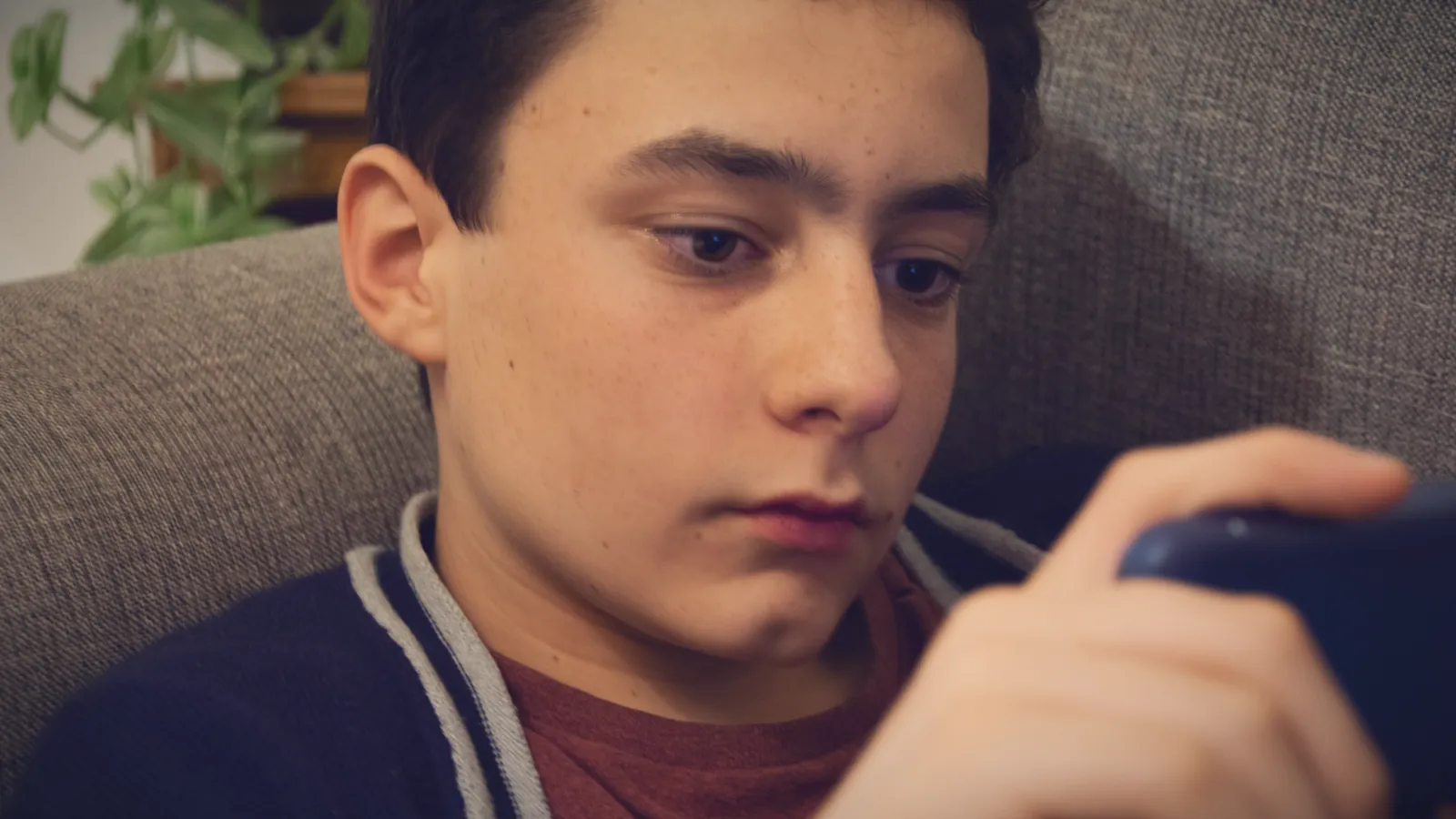 A teenage boy on the sofa completely absorbed in his phone