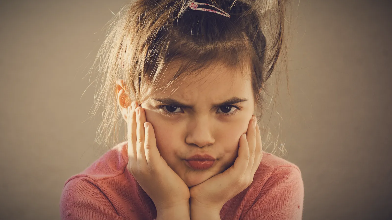 A young girl frowning with her face in her hands, cross and fed up